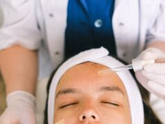 Top view skilled female cosmetologist in uniform and gloves applying essential oil on young woman face skin while working in contemporary spa center