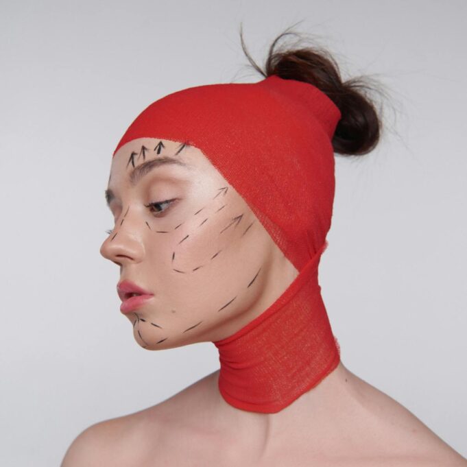 Artistic portrait showing cosmetic surgery markings on model in red wrap.